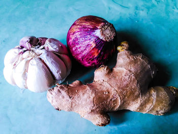 Close-up of ginger by garlic bulb and onion on blue table