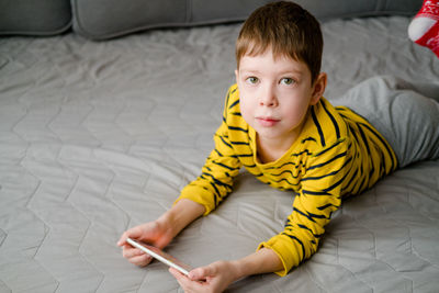 A teenage boy lies on the couch with a phone in his hands. the child plays at home in the phone.