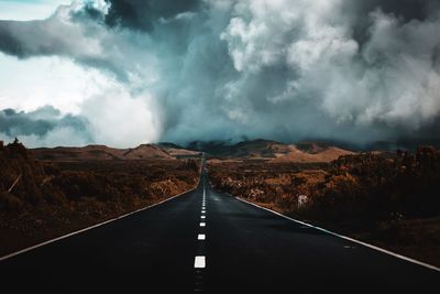 Diminishing perspective of empty road passing landscape against cloudy sky