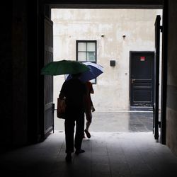 Rear view of men walking with umbrellas on doorway