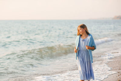 Stylish teenge kid girl 12-14 year old wear trendy dress and knit blue cardigan walk over sea 