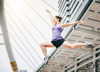 Low angle view of athlete with arms raised and legs apart jumping in city