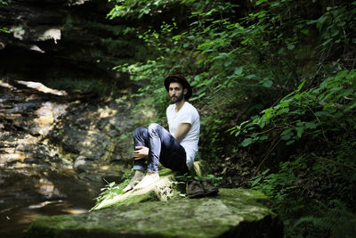 Young man sitting on rock in forest