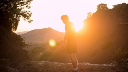 Side view of woman standing on land against sky during sunset