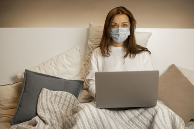 Portrait of woman wearing mask working on laptop at home