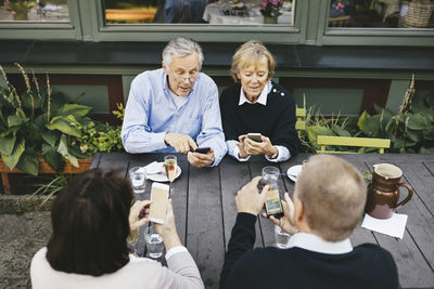 Two senior couples using mobile phones at table of outdoor restaurant