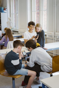 Male and female students using smart phones while sitting at desk in classroom