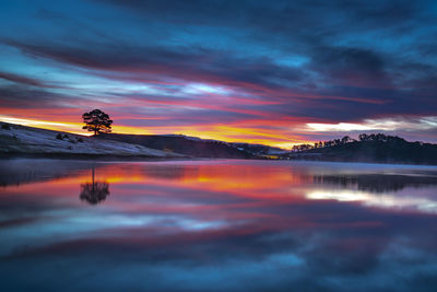 Scenic view of lake against dramatic sky during sunset