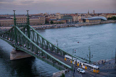 Green metallic bridge over river in city against sky