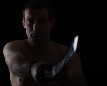 Close-up portrait of angry man holding sword in darkroom