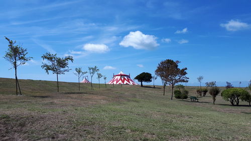 Trees on field and circus tent against sky
