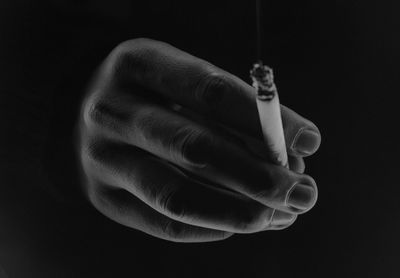 Close-up of hand holding cigarette against black background