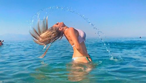 Side view of woman tossing wet hair in sea against sky