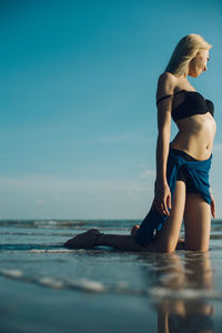 Low angle view of seductive woman at beach against blue sky