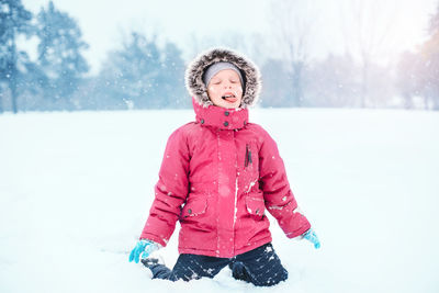 Girl kneeling on snow covered field during winter