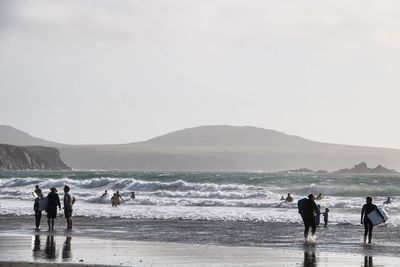 People enjoying at beach by mountain against clear sky