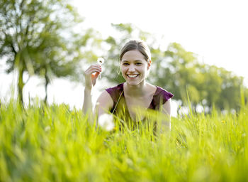 Portrait of smiling woman holding dandelion on grassy field