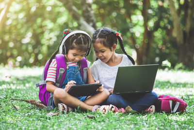 Schoolgirls using laptop and digital tablet while sitting in park