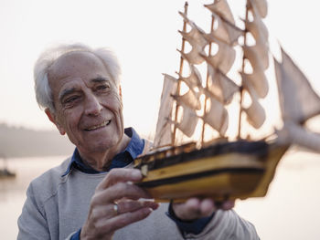 Smiling man examining sailing ship toy while standing outdoors