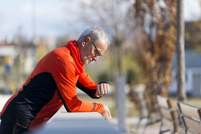 Senior man checking time while standing by retaining wall