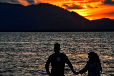 Silhouette men on beach against sky during sunset