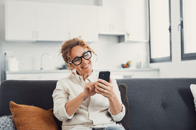 Young woman using mobile phone while sitting on sofa at home