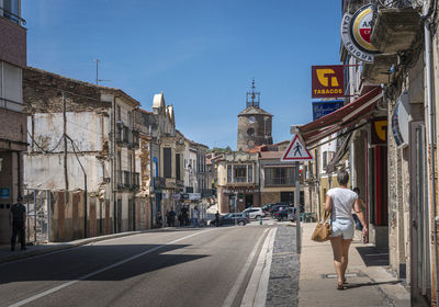 Woman walking on road amidst buildings in city