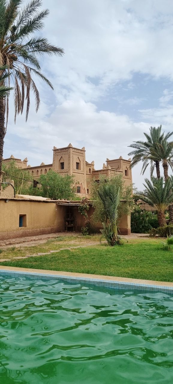 palm tree, architecture, tropical climate, built structure, building exterior, tree, building, water, vacation, plant, nature, house, sky, cloud, residential district, travel destinations, sea, no people, mansion, home, land, outdoors, estate, travel, coconut palm tree, holiday, day, tourist resort, trip, tourism, swimming pool, coast, environment, grass, city, shore, wealth, date palm tree