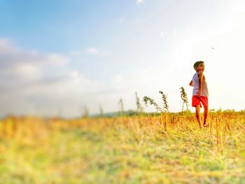 Rear view of boy walking on field against cloudy sky