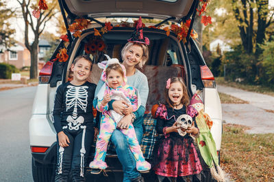 Smiling mother and kids sitting by car trunk