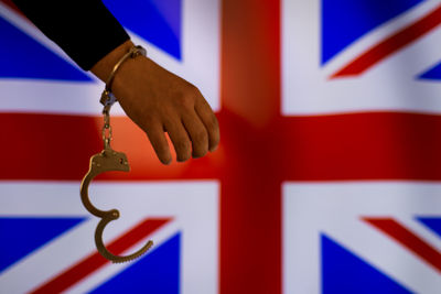 Cropped hand of male criminal with handcuffs against british flag