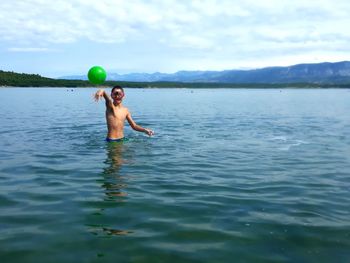 Shirtless boy playing with ball in sea against sky