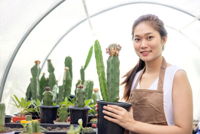 Portrait of smiling young woman using phone while sitting on potted plant