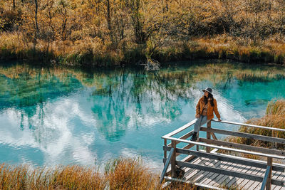 Woman sitting on wooden deck by turquoise lake surrounded by idyllic nature in autumn.