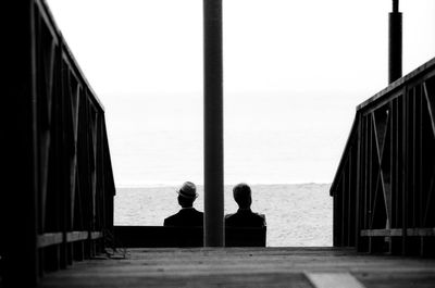 Rear view of silhouette people sitting on beach against clear sky
