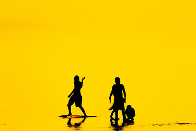 Silhouette people walking on street against orange sky