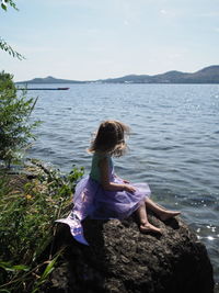 Rear view of woman sitting on rock by lake