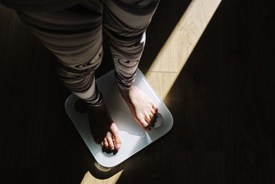 Young woman standing on weight scale in dark at home