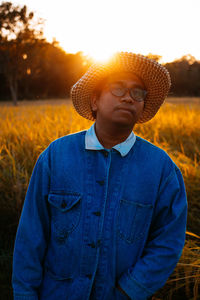 Man wearing hat standing on field against sky during sunset