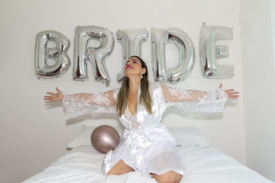 Woman sitting on bed against white wall with writing bride. 