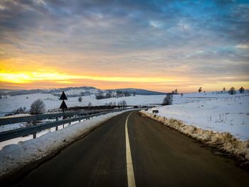 Snow covered road against sky during sunset