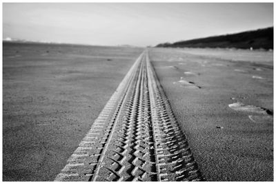 Surface level of railroad tracks on beach against sky