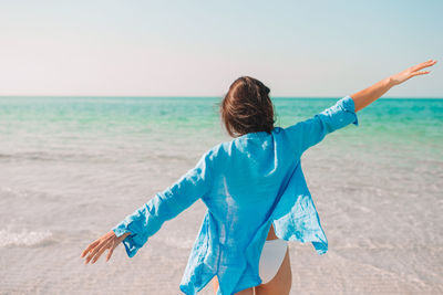 Rear view of woman standing at beach against sky