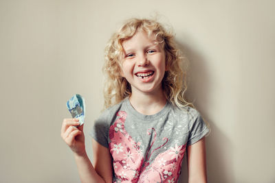 Portrait of laughing girl holding banknote standing against wall