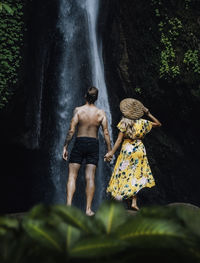 Rear view of man standing by waterfall in forest