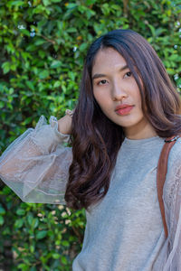 Portrait of young woman while standing against plants at park