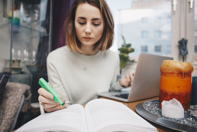 Young woman using smart phone while sitting in laptop