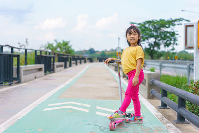 Little child girl to ride scooter in outdoor sports ground on sunny summer day. 