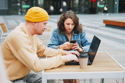 Stylish young couple freelancers working on laptop in street cafe