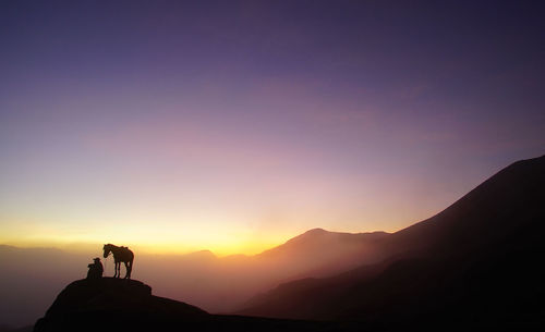 Silhouette man and horse on mountain cliff